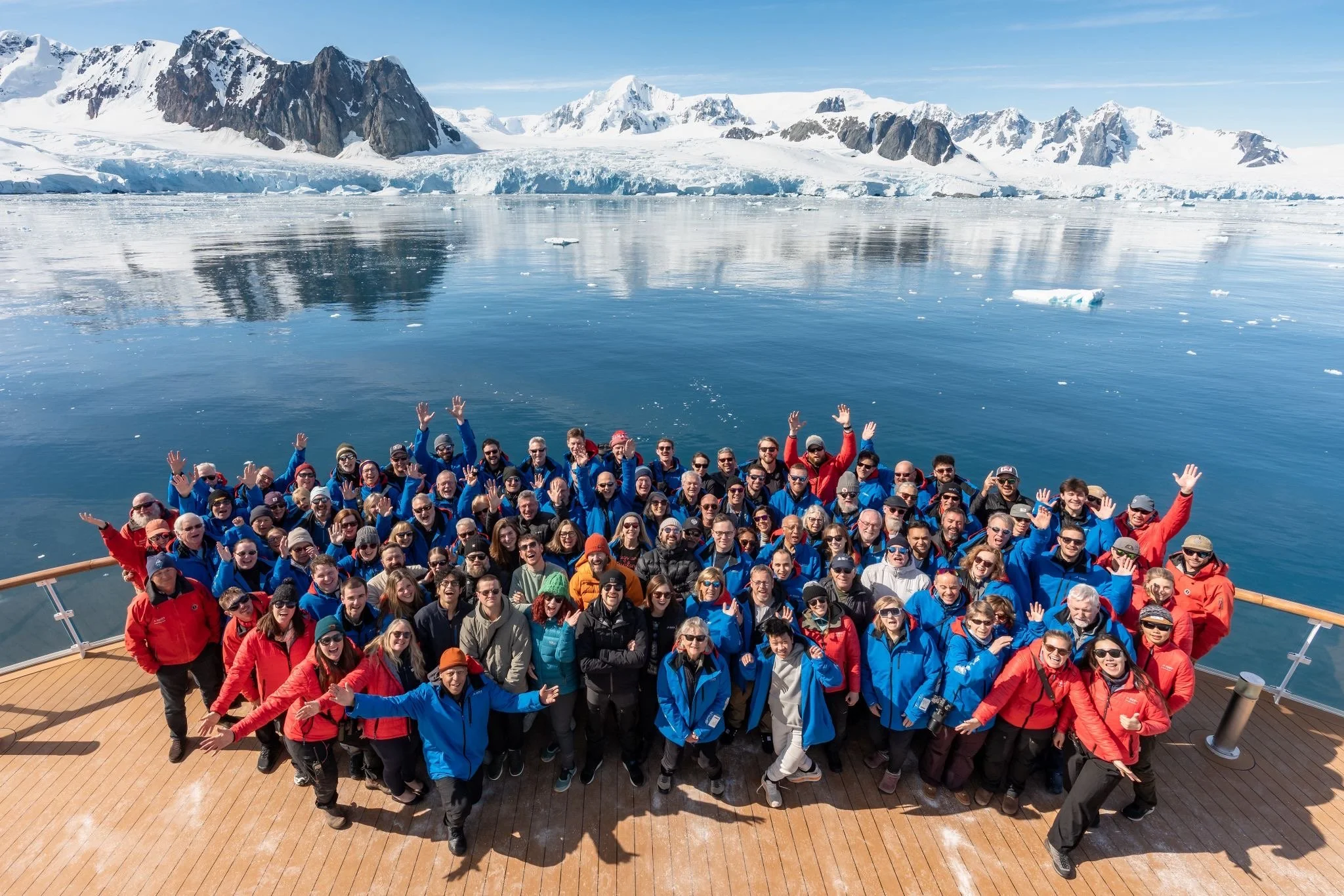 A photograph of a wildlife photography workshop group on the deck of a ship in icy, mountainous Antarctic landscape, many waving and smiling.