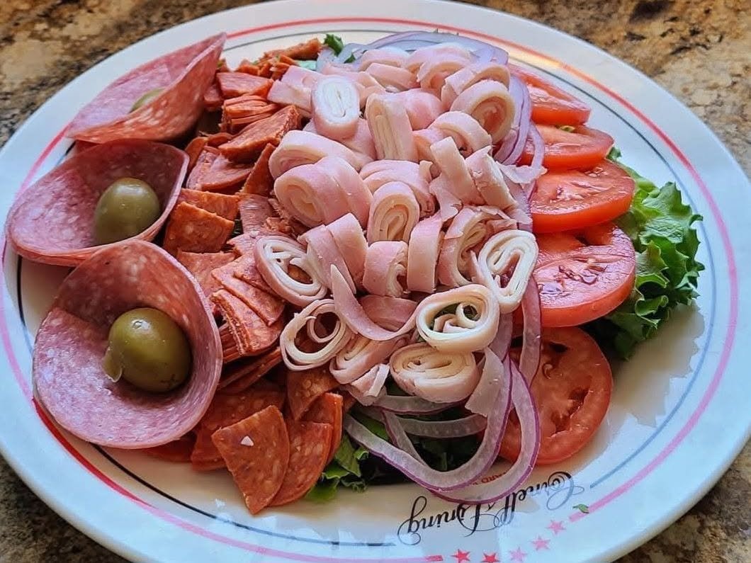 Plate with assorted deli meats, sliced tomatoes, onions, lettuce, and green olives.