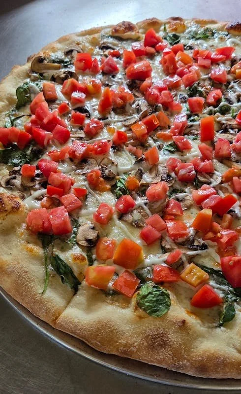 Close-up of a vegetable pizza with chopped tomatoes, mushrooms, spinach, and cheese on a golden crust.