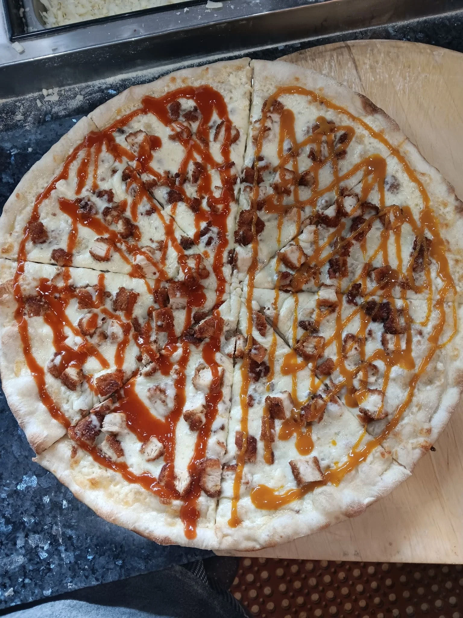 Pizza cut into slices on a wooden board, topped with different sauces and small pieces of cooked chicken.