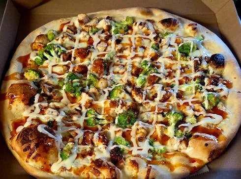 Pizza topped with broccoli, chicken, cheese, and drizzle of sauce.