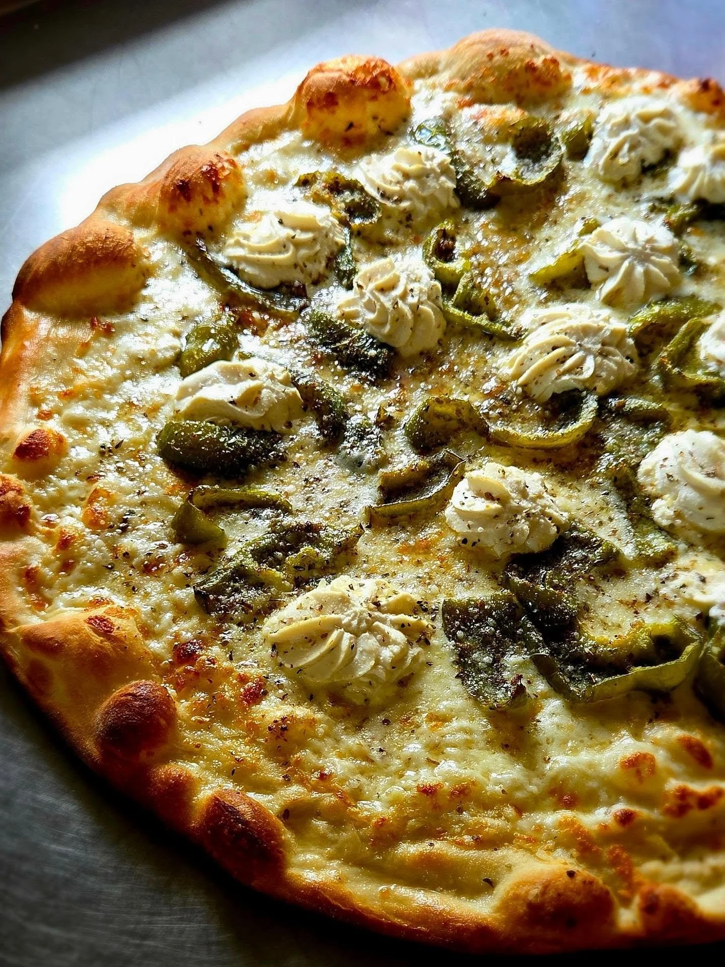A close-up of a slice of pizza with cheese, green peppers, and mushrooms on a dark surface.