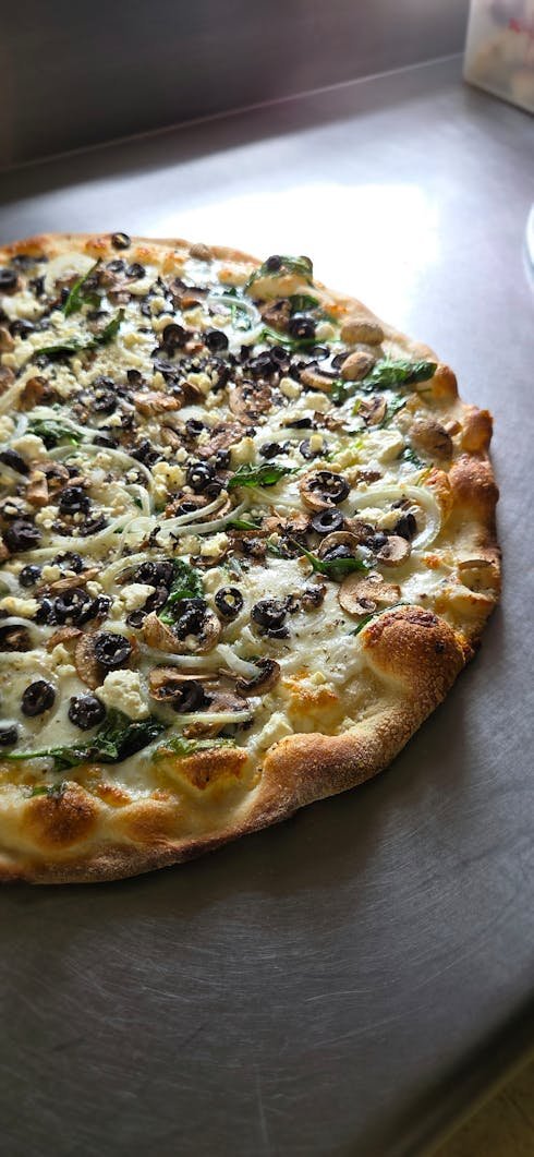 A pizza with cheese, black olives, mushrooms, and spinach on a crust.