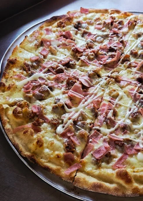 Close-up of a half-eaten pizza with cheese, ham, and sausage on a round tray.