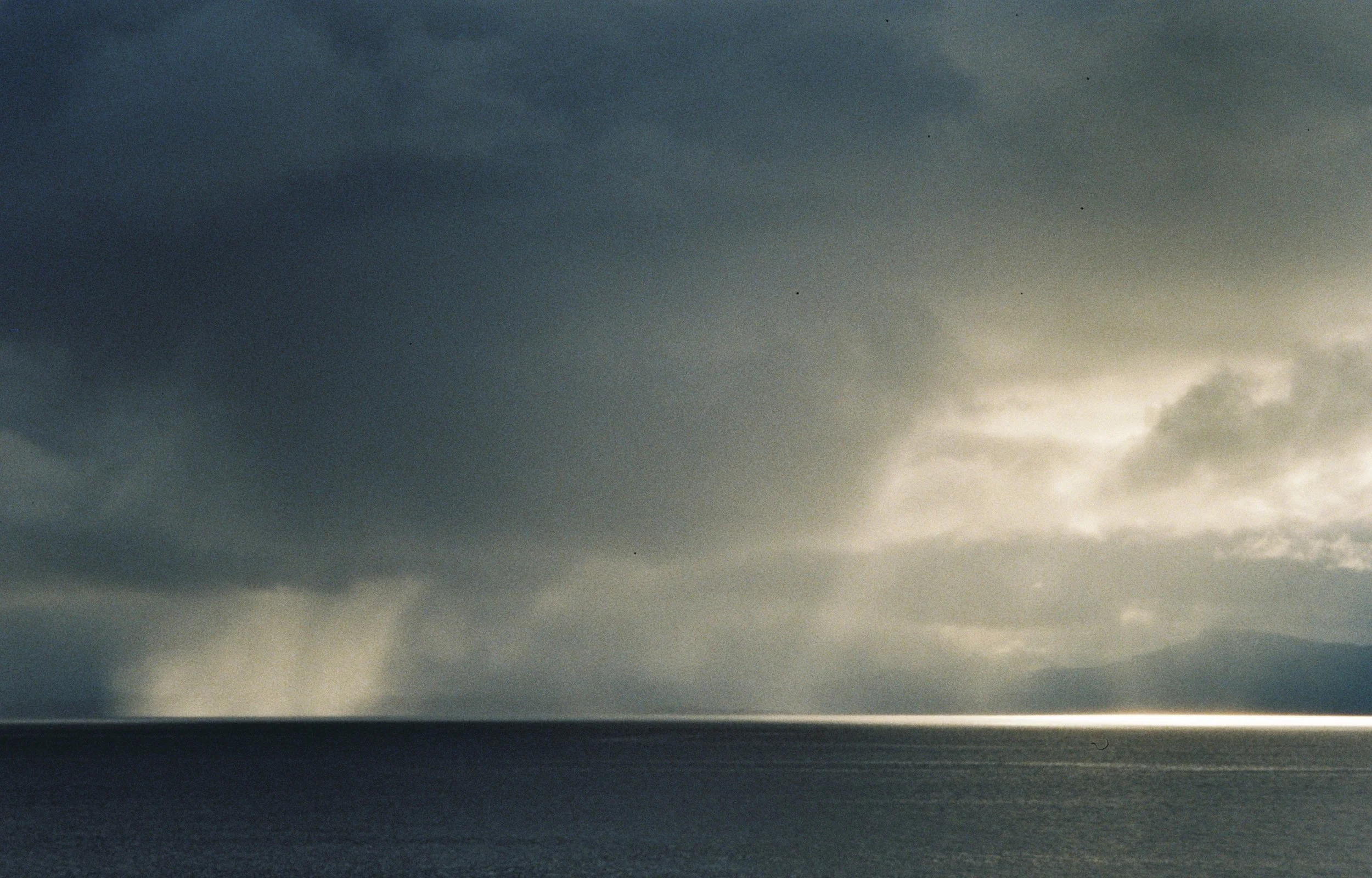 A landscape photo of a vast ocean with a dark and stormy sky above, and the horizon line separating the water from the cloudy sky.
