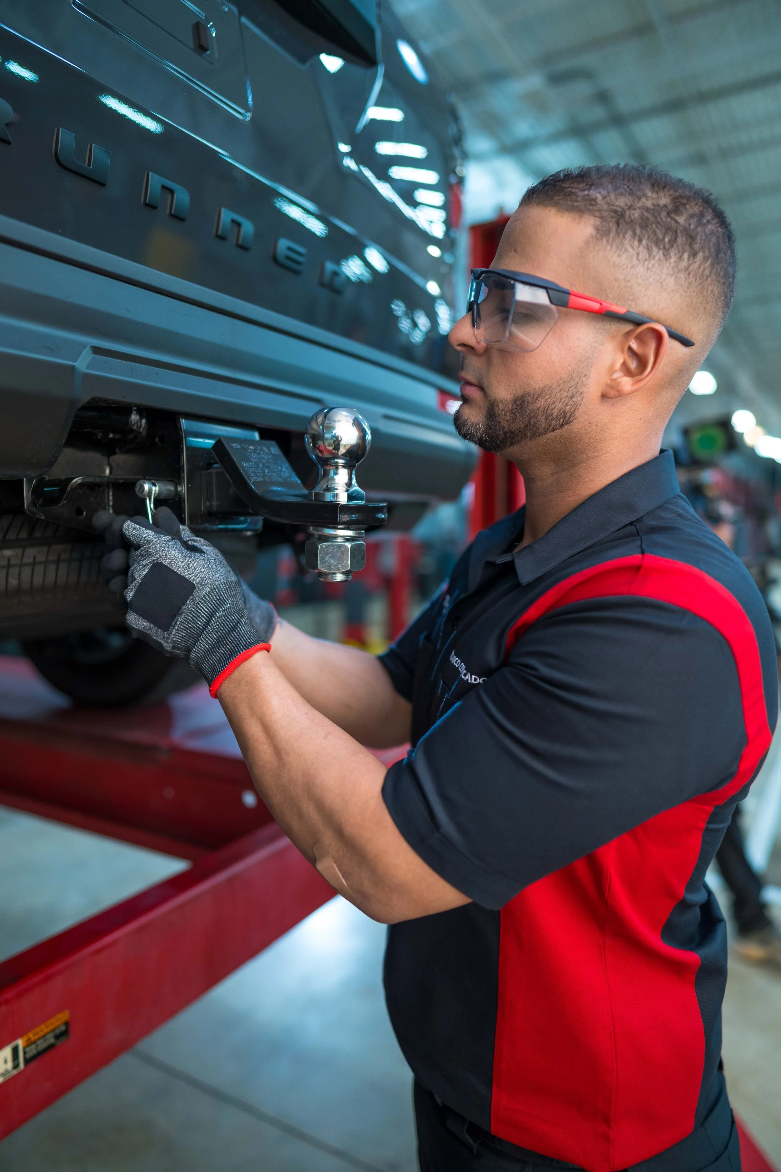 Toyota technician installing a tow hitch and ball mount on the rear of a 4Runner.