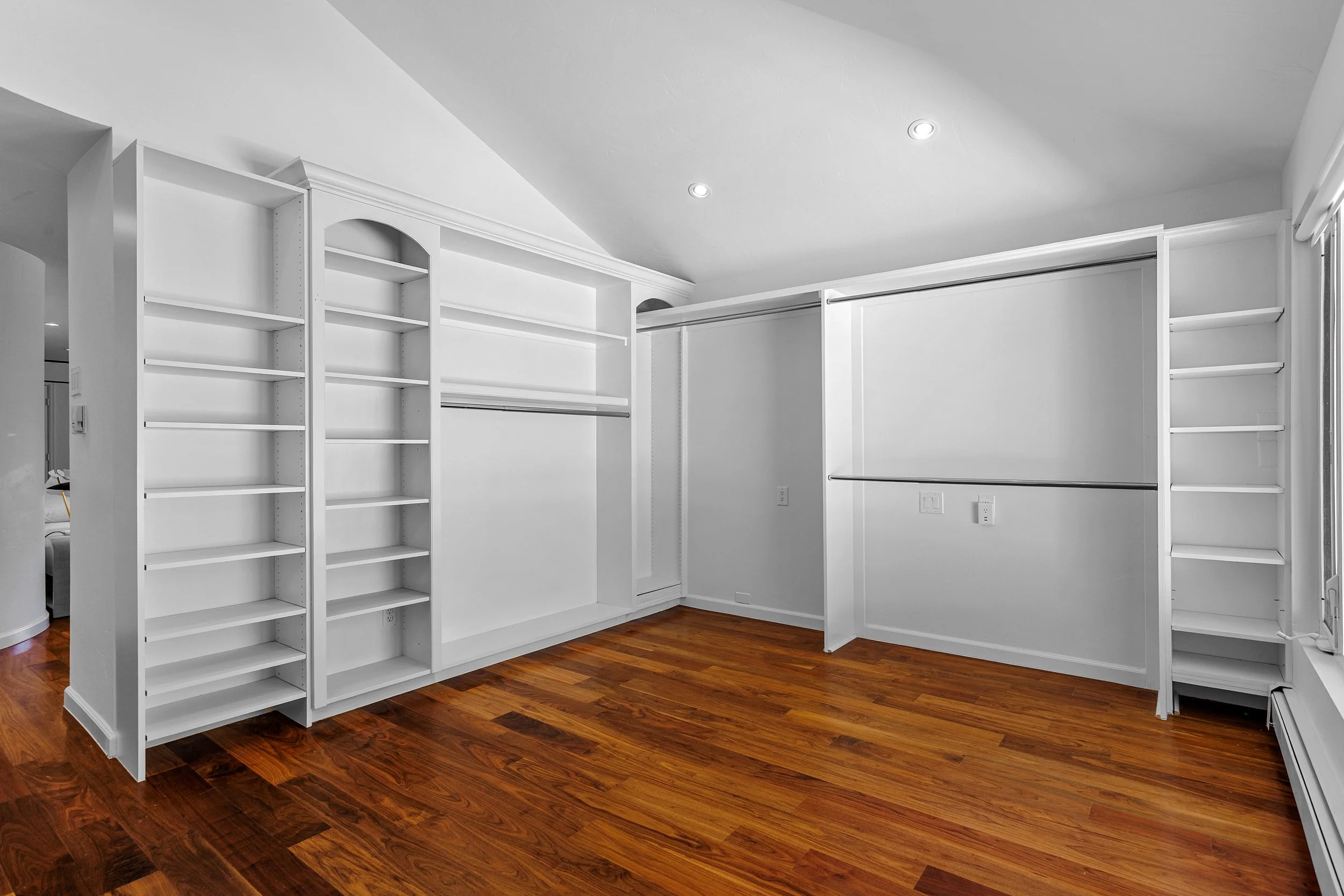Empty white walk-in closet with built-in shelves, hanging rods, and hardwood flooring.