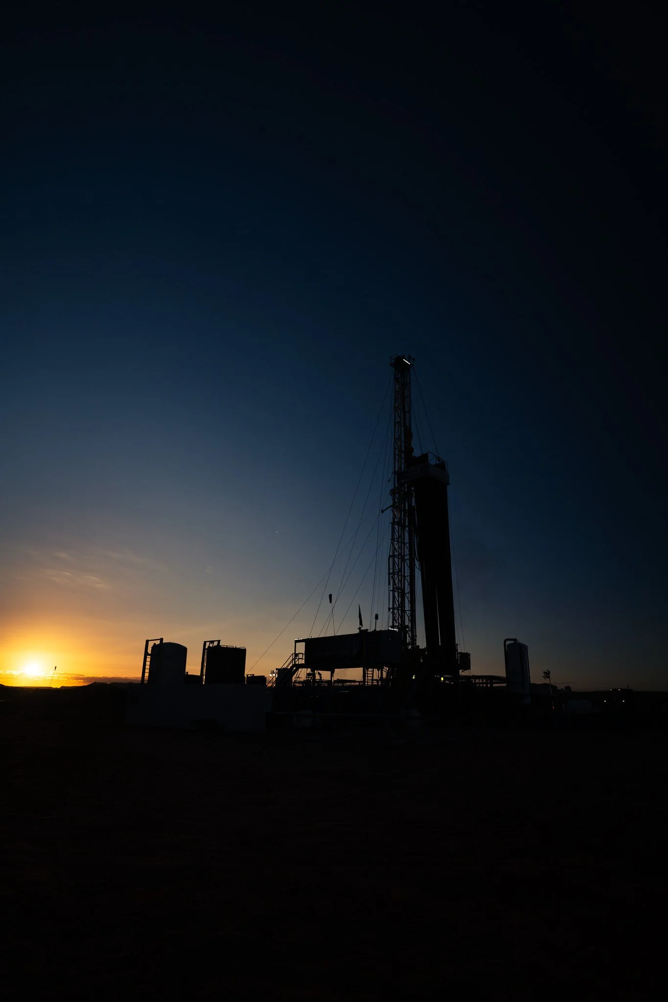 Silhouette of a potash well against a sunset sky with the sun visible on the horizon and a dark sky above.