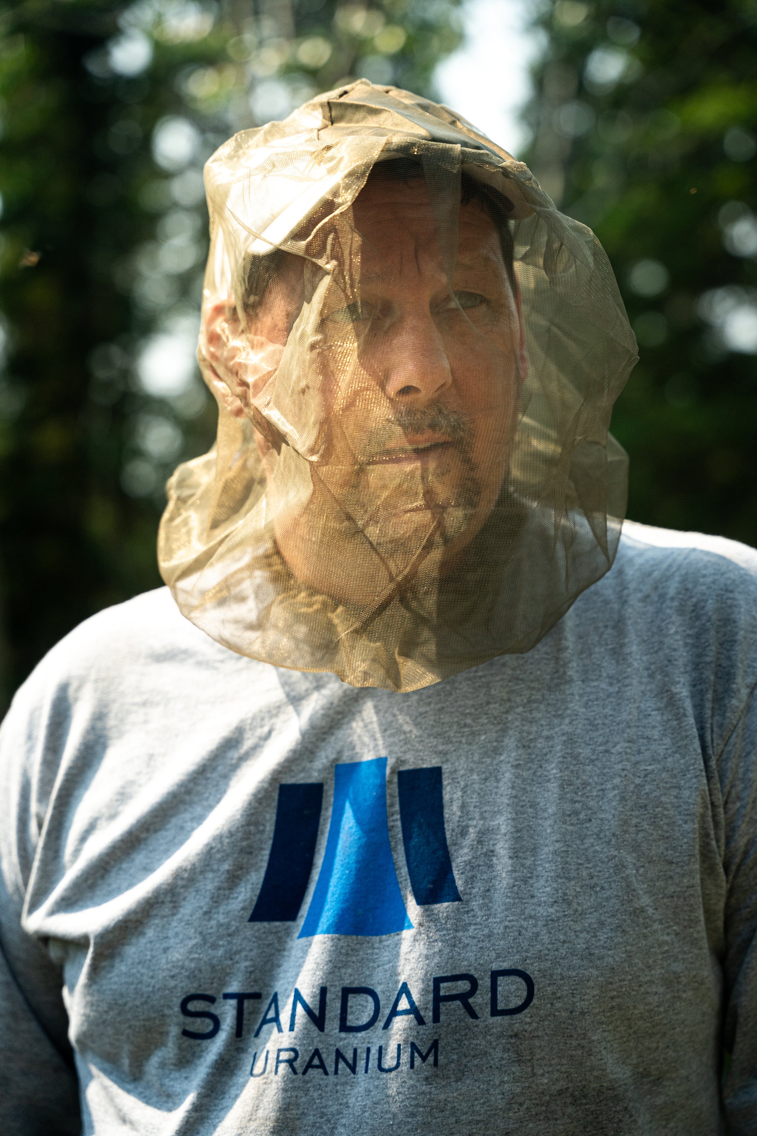 A person wearing a gray t-shirt with blue text and a large mesh net over their head outdoors during daytime.