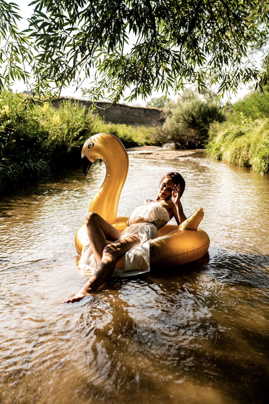 boudoir photoshoot on gold flamingo float in a river, surrounded by greenery. Healing your inner child through play, self discovery for women. 