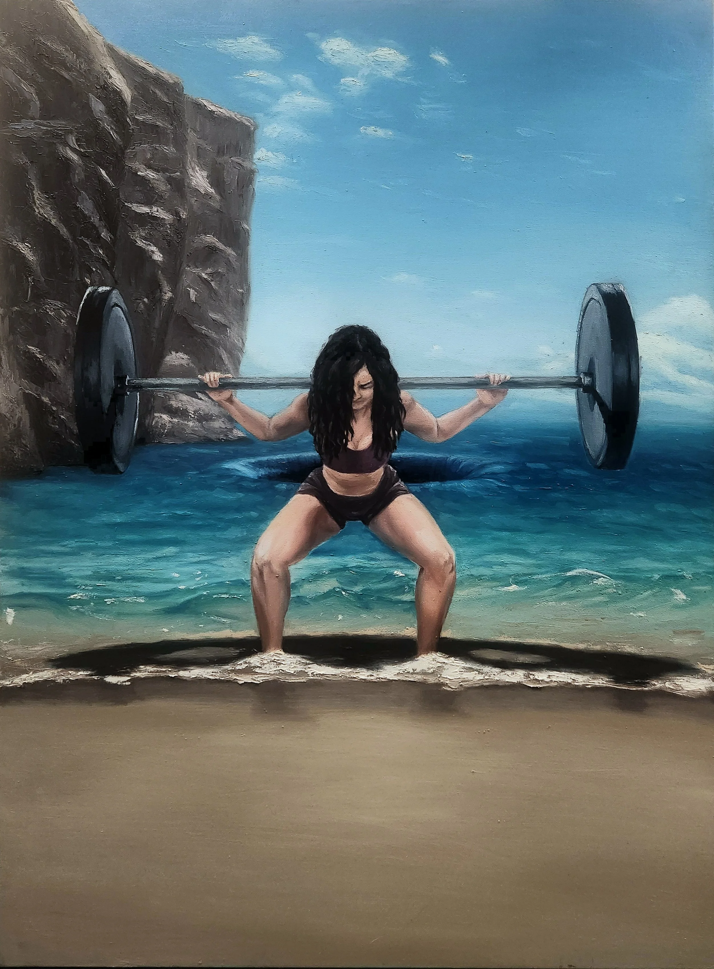 A woman with long dark hair, wearing a sports bra and shorts, squatting while holding a barbell with weights at the beach, near water and rocks, under a partly cloudy sky.
