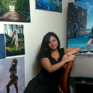 Woman with long dark hair sitting next to a table in an art gallery, surrounded by landscape paintings on the wall.