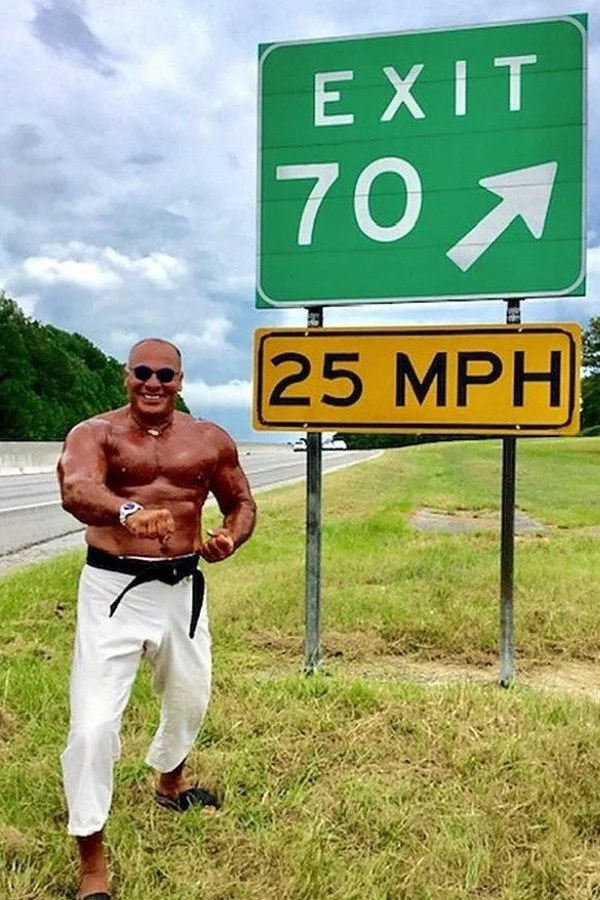 Nabil at age 70 beside an Exit 70 highway sign