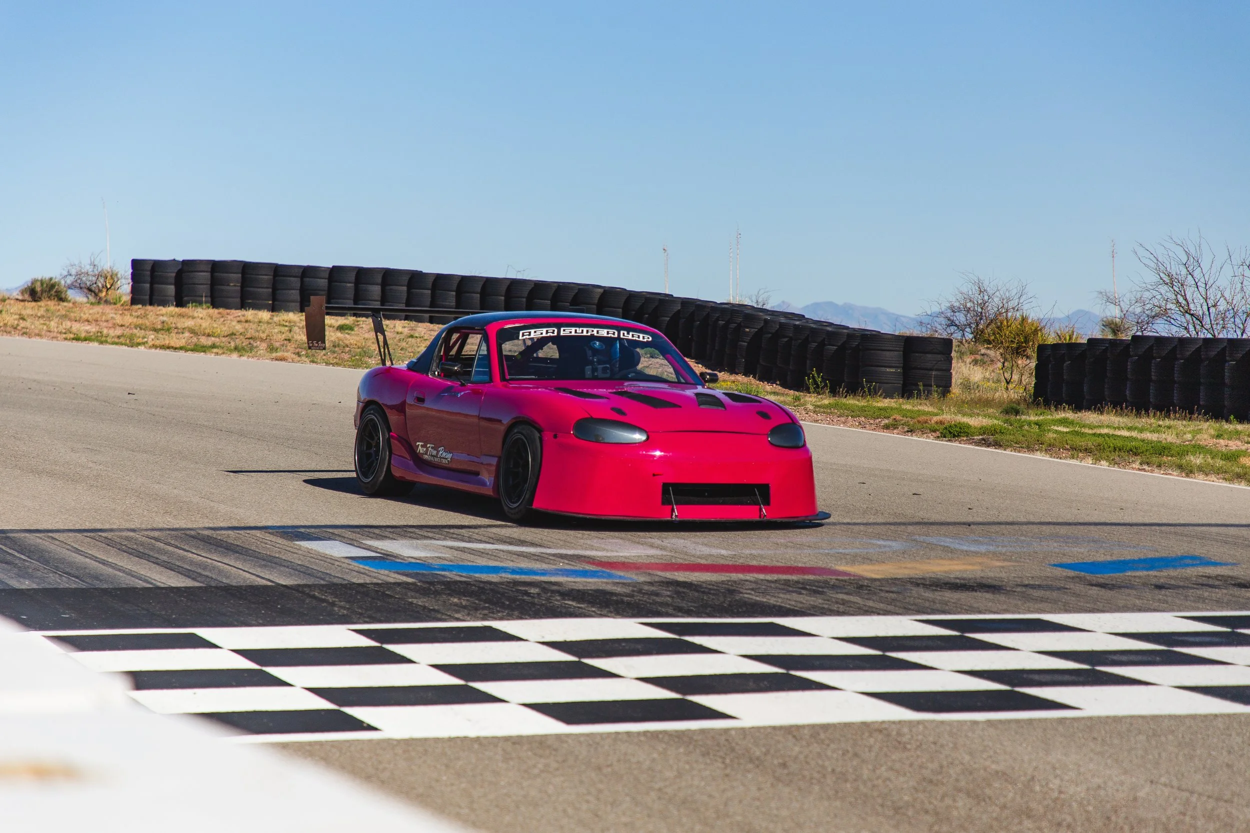 Pink race car on a racetrack, crossing the finish line with a black and white checkered pattern.