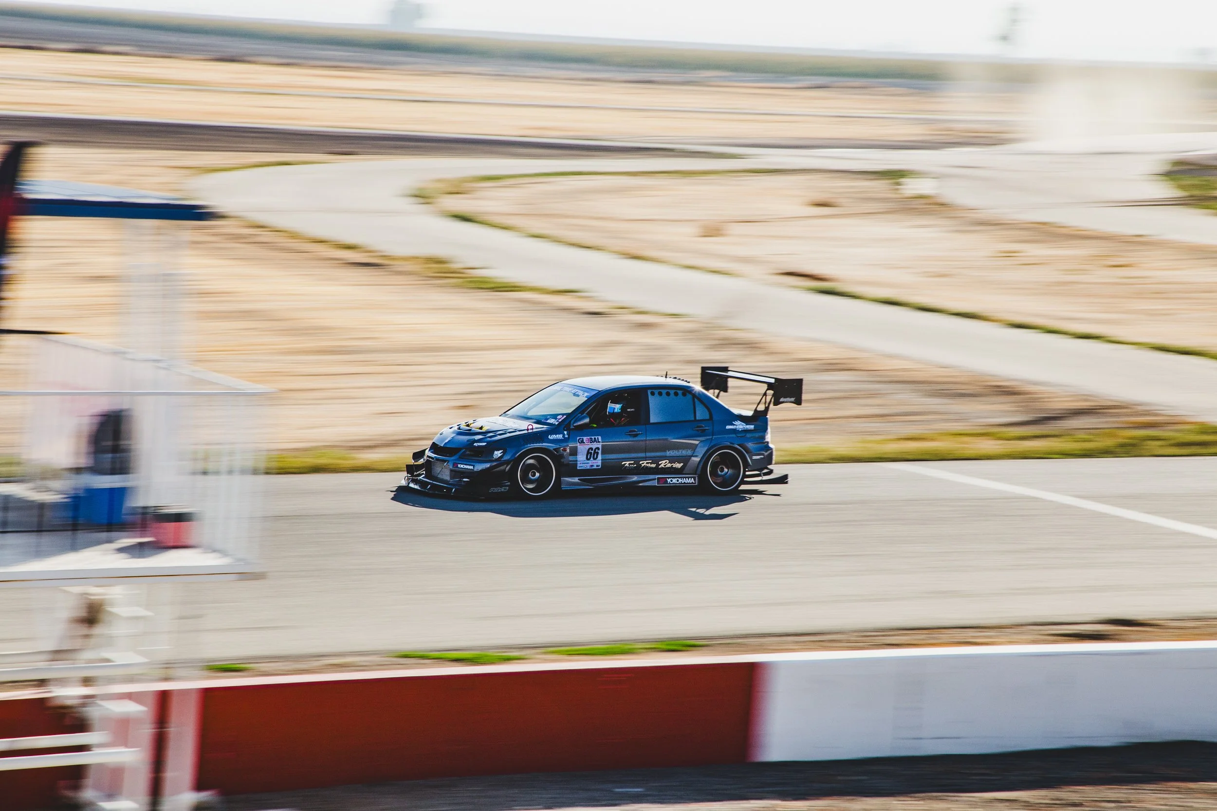 A black race car with the number 66 on the side speeding on a race track during a race with motion blur in the background.