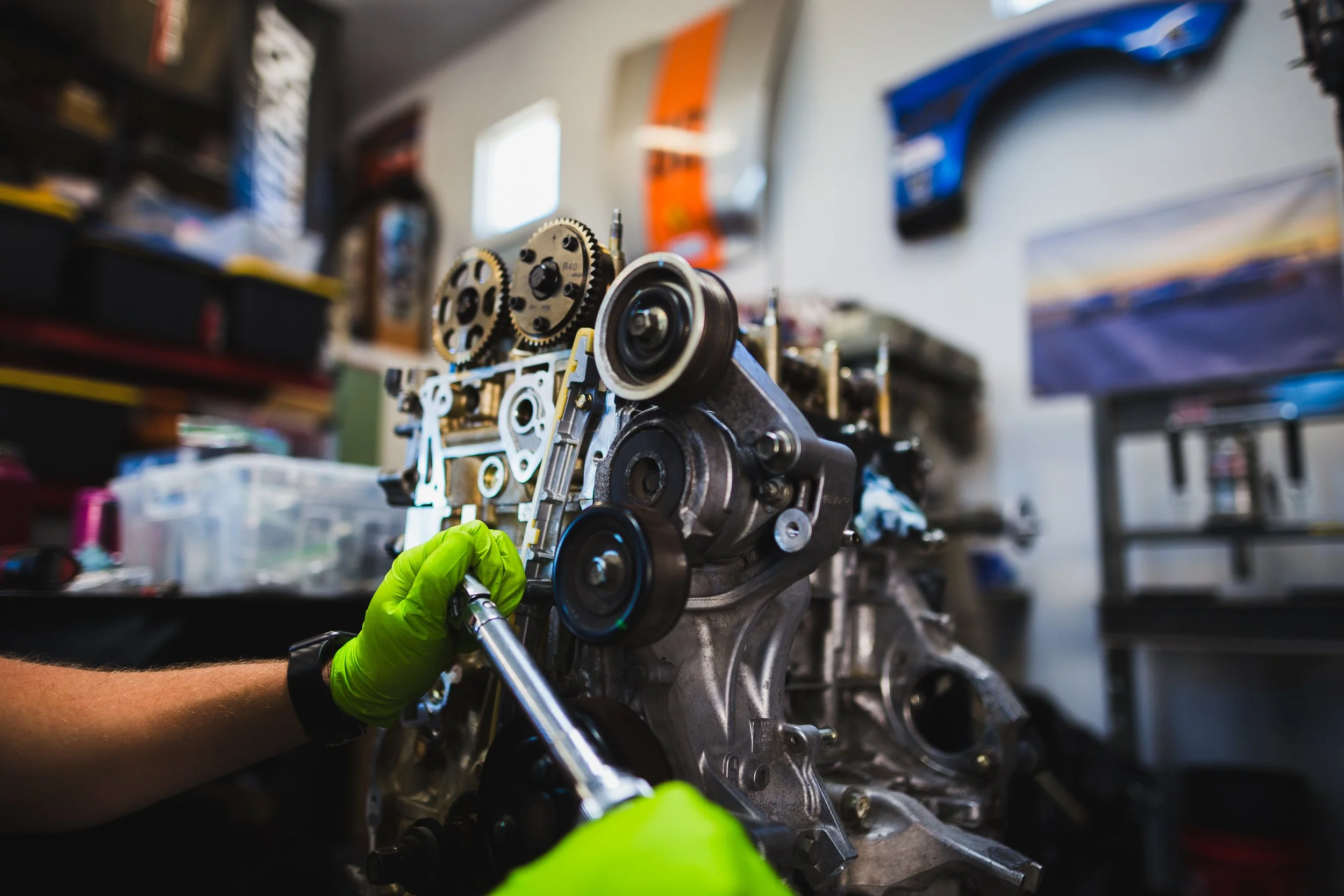 Mechanic wearing neon yellow gloves working on an engine in a workshop.
