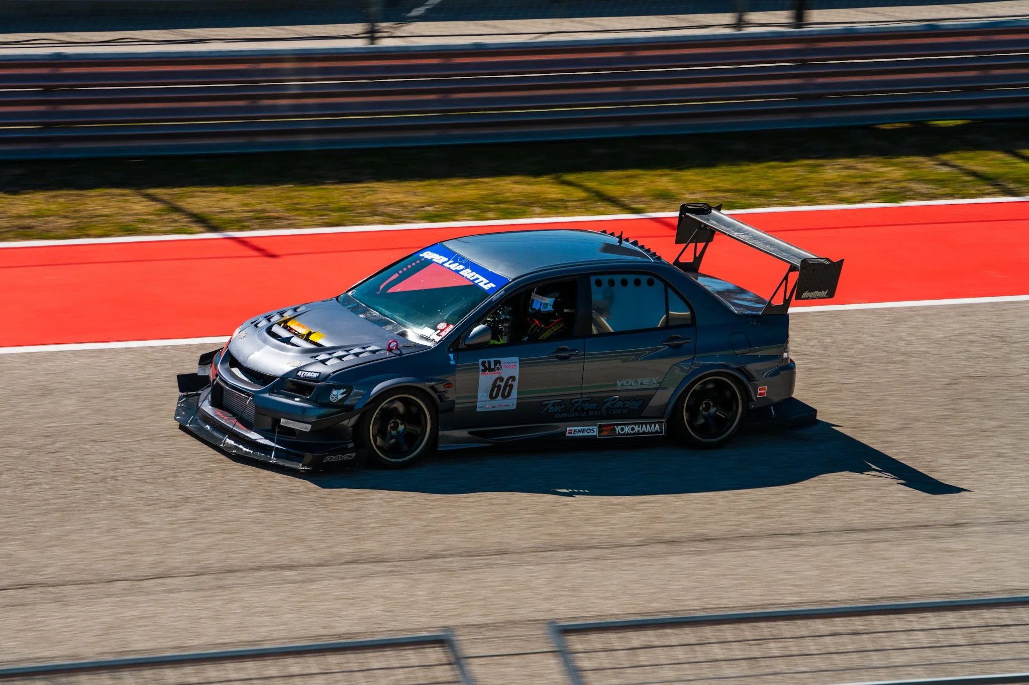 A race car on a racetrack, featuring a black body with sponsor logos, a prominent rear wing, and the number 66 on the side, in a racing event setting.
