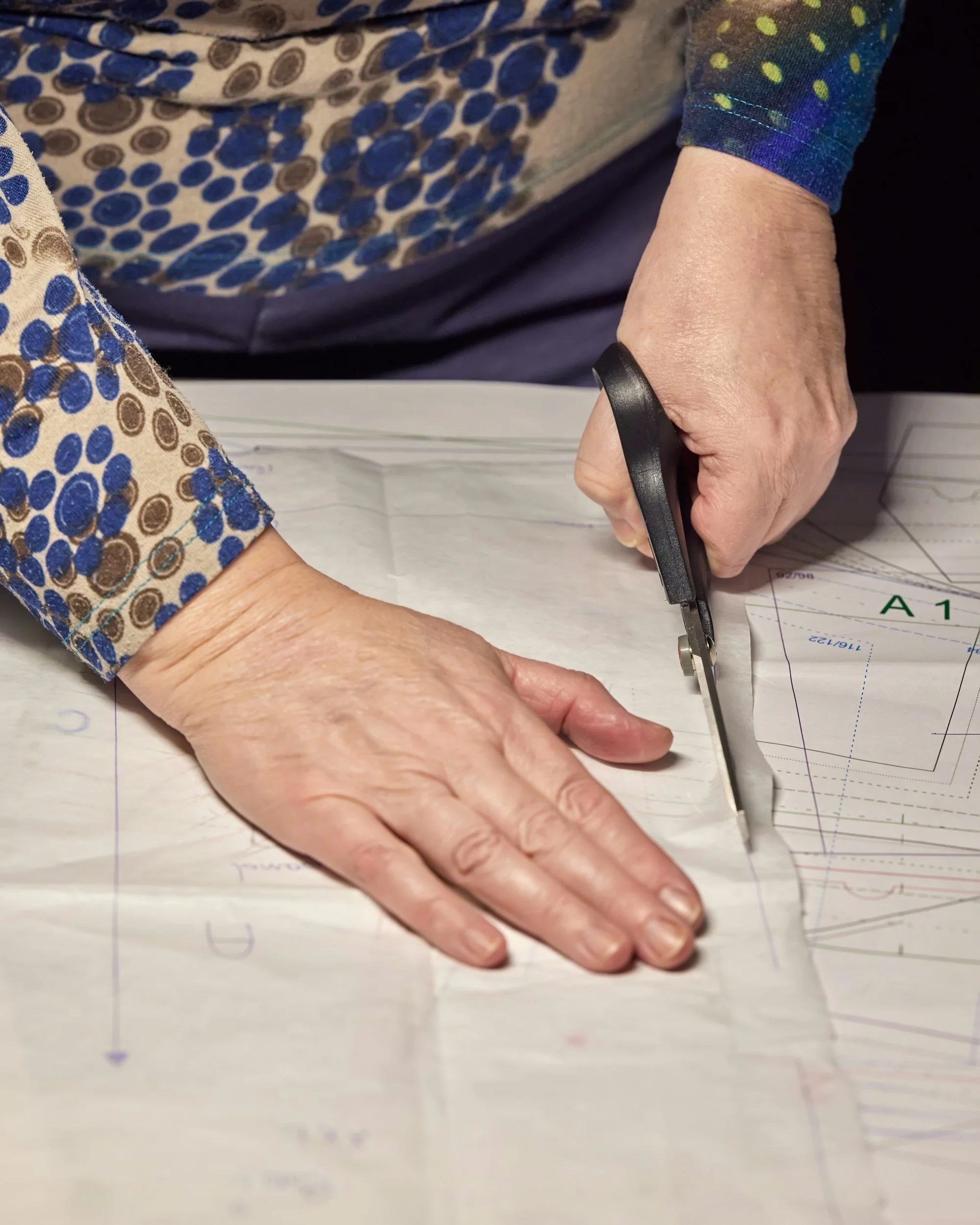 A person cutting paper with scissors. The person is wearing a patterned shirt and has a ring on their finger.