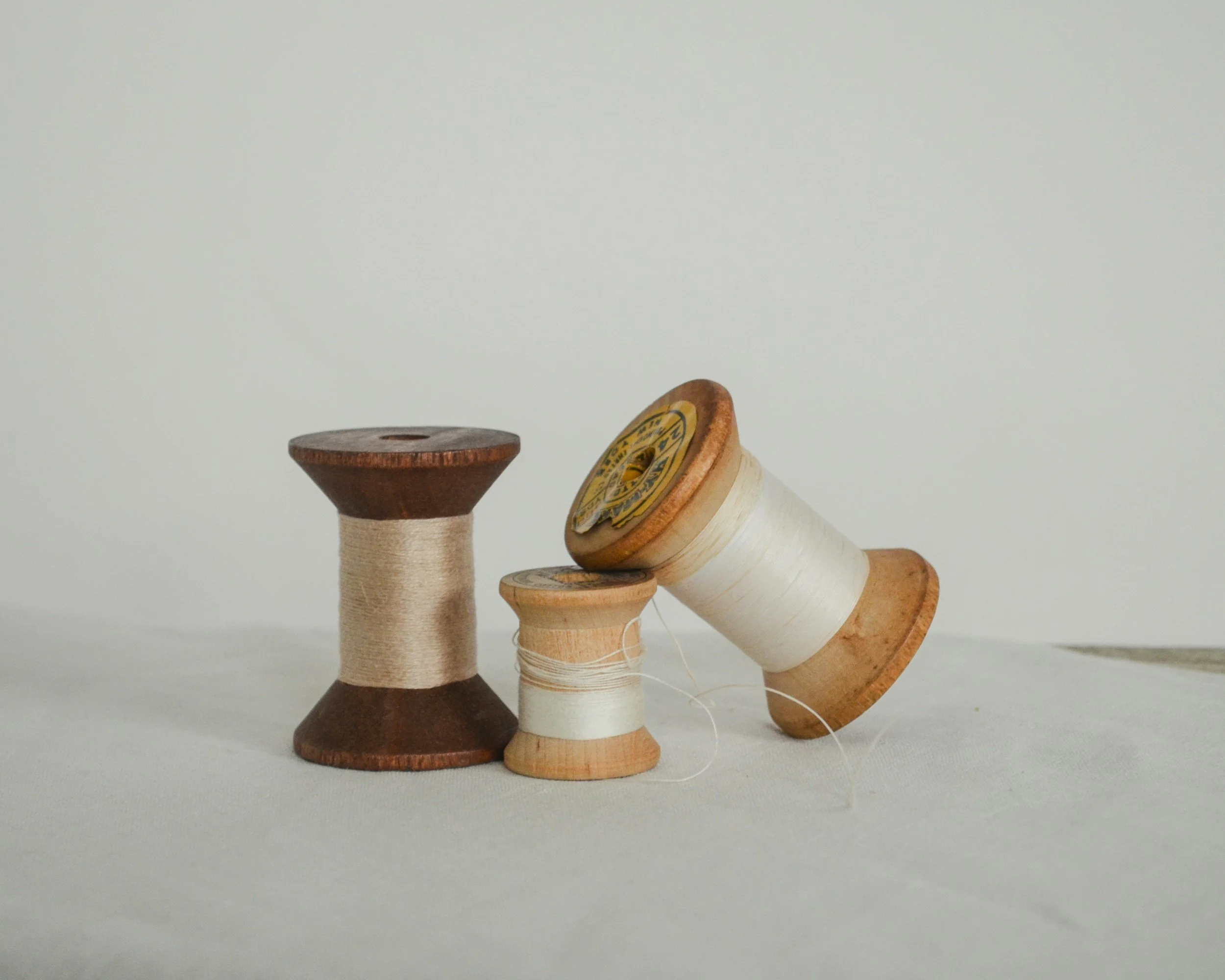 Four vintage wooden thread spools with different colors and sizes arranged in a line on a white surface against a plain light background.