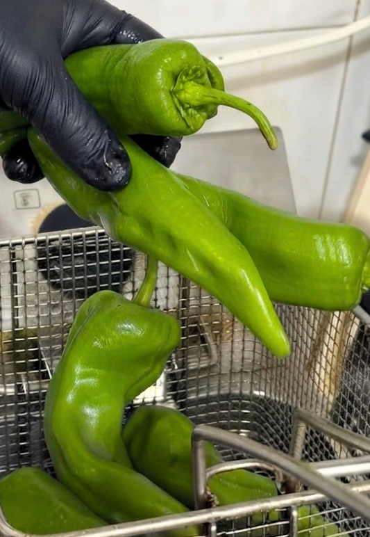 Mano con guantes negros sosteniendo pimientos verdes en una tienda o cocina.
