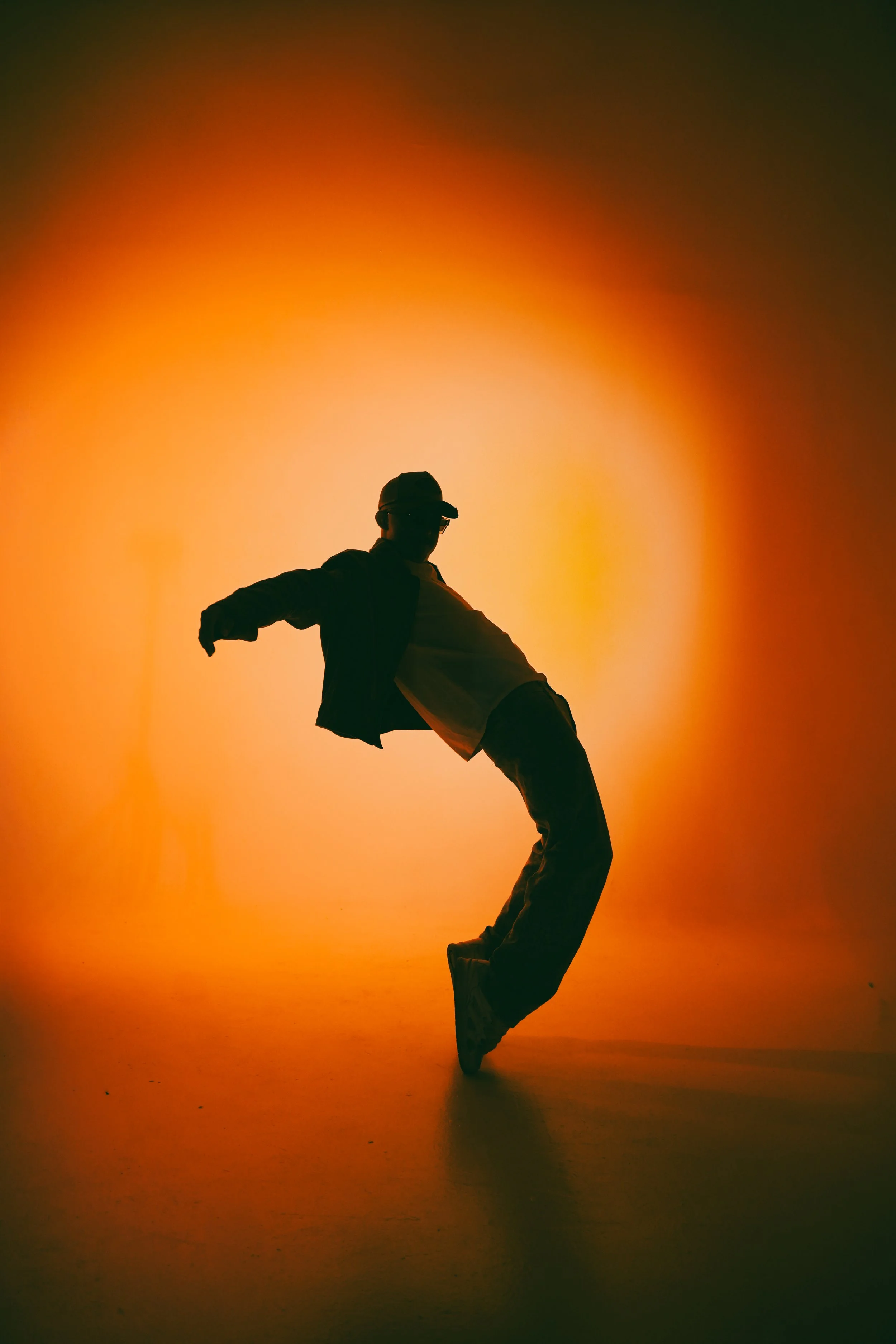 Silhouette of a person dancing or jumping against a vibrant, warm-colored background with orange and yellow hues.