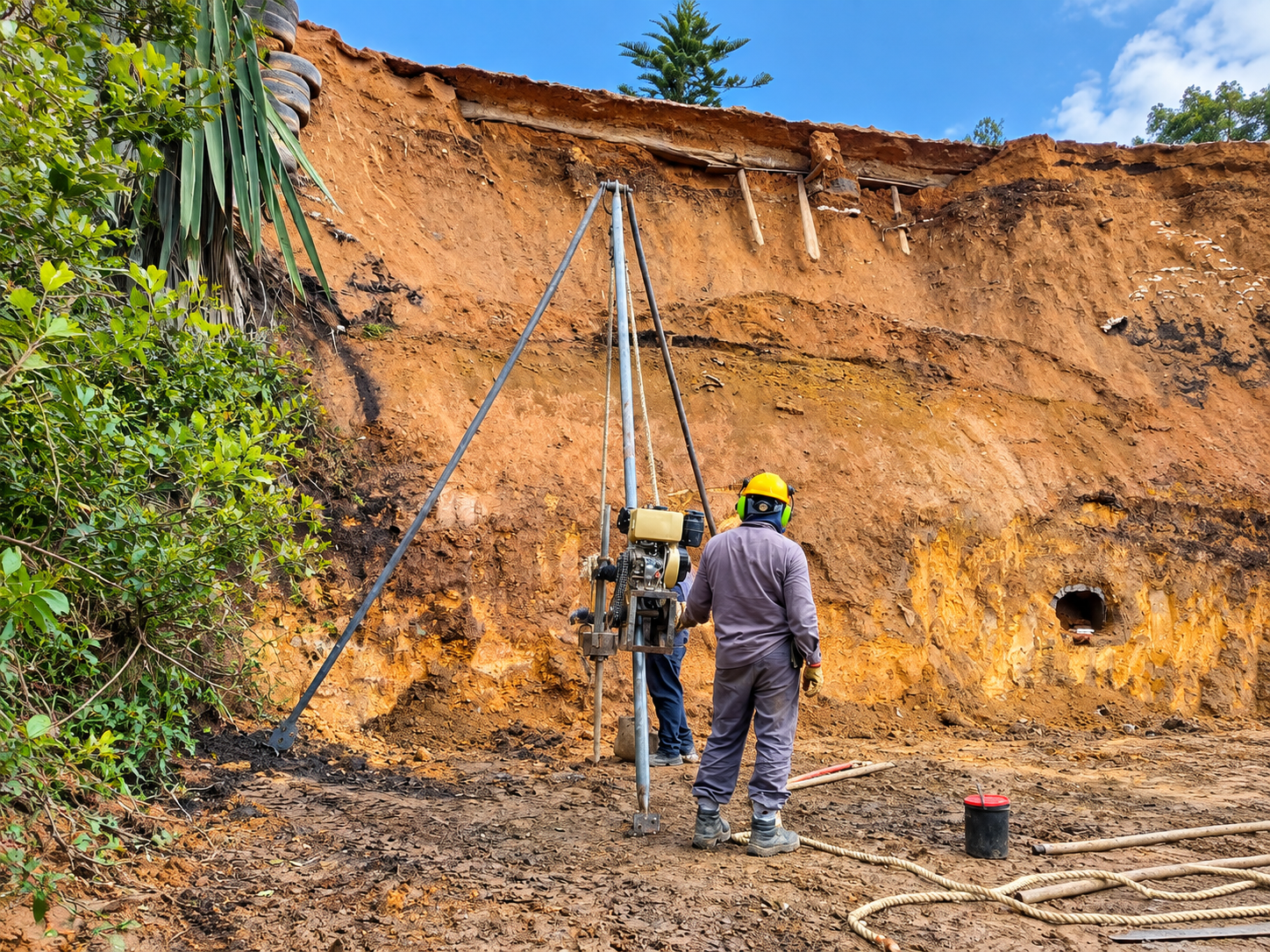 Técnico trabajando en excavación en una zona de tierra erosionada, con maquinaria y equipo de seguridad en un área al aire libre.