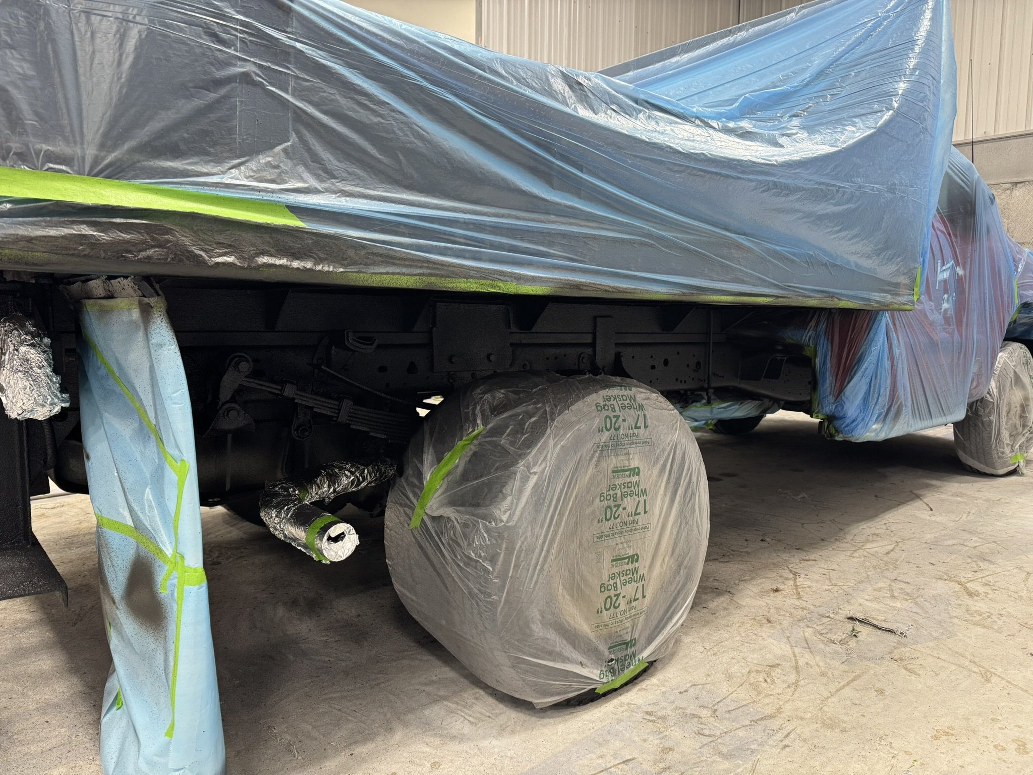 A vehicle with parts covered in plastic and masking tape, with a large bag of drywall joint compound in front of it inside a garage or workshop.