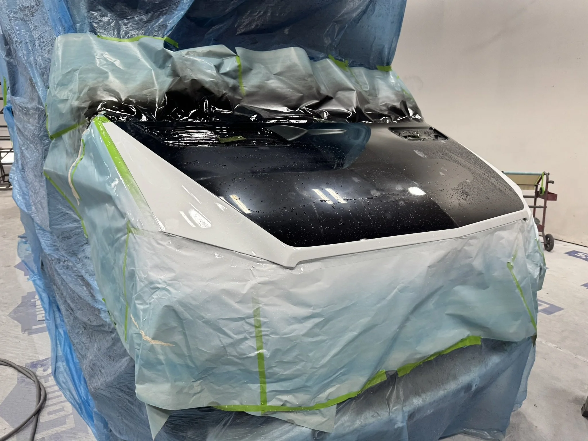 A car covered with masking paper and plastic, and being prepared for painting in a workshop.