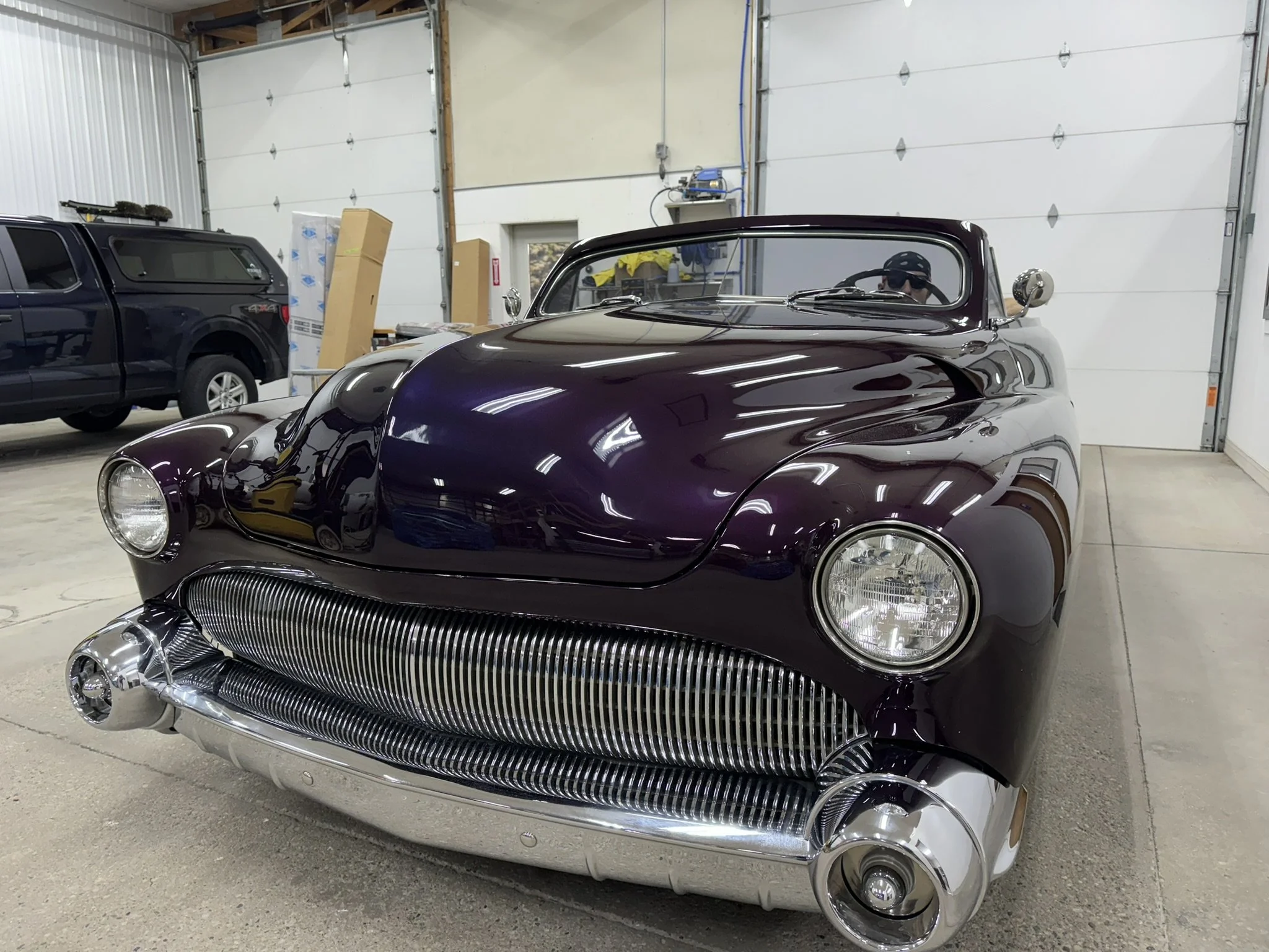 A vintage maroon sports car with a shiny chrome grill and rounded headlights in a garage.