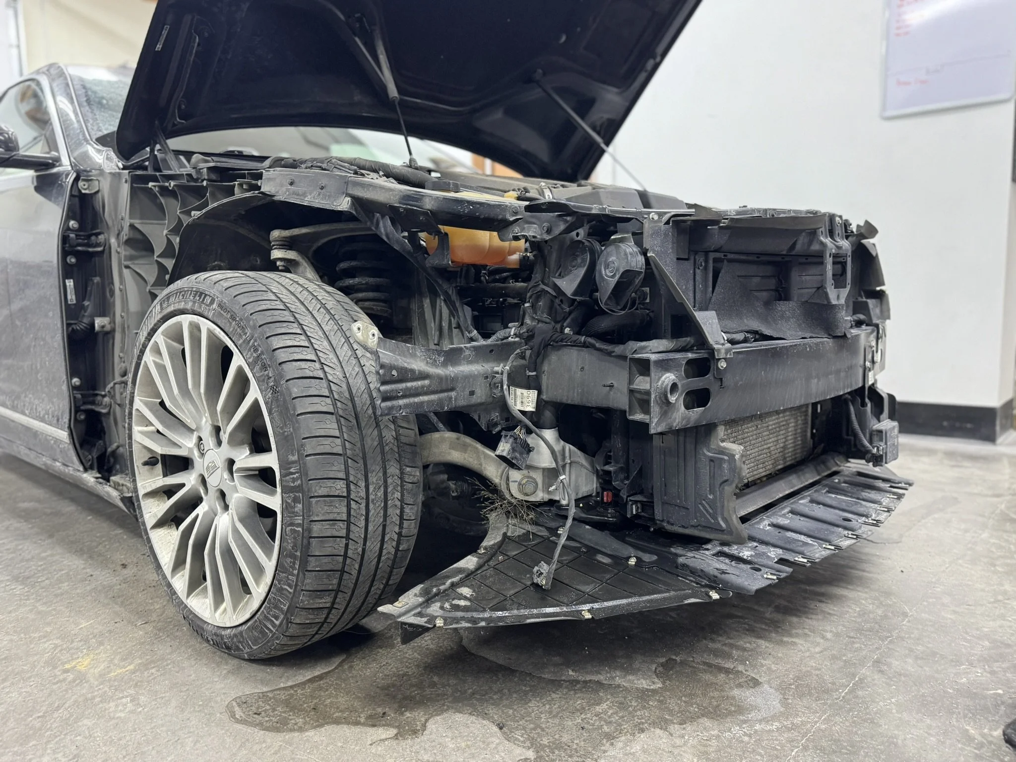 Car with front end severely damaged, hood open, missing parts, and exposing internal components.