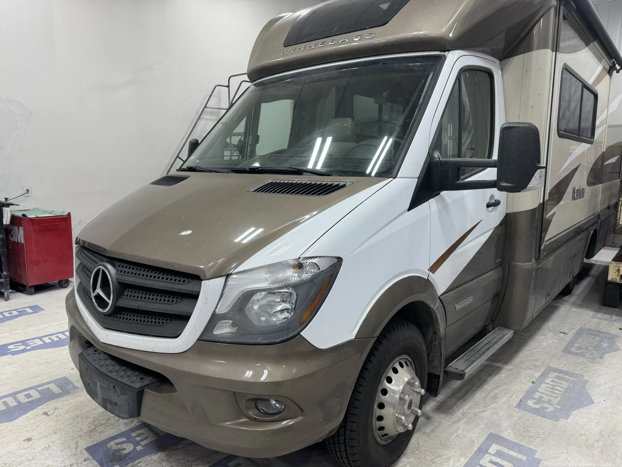 A Winnebago motorhome parked in an indoor space, with a tan and white color scheme and large side mirrors.