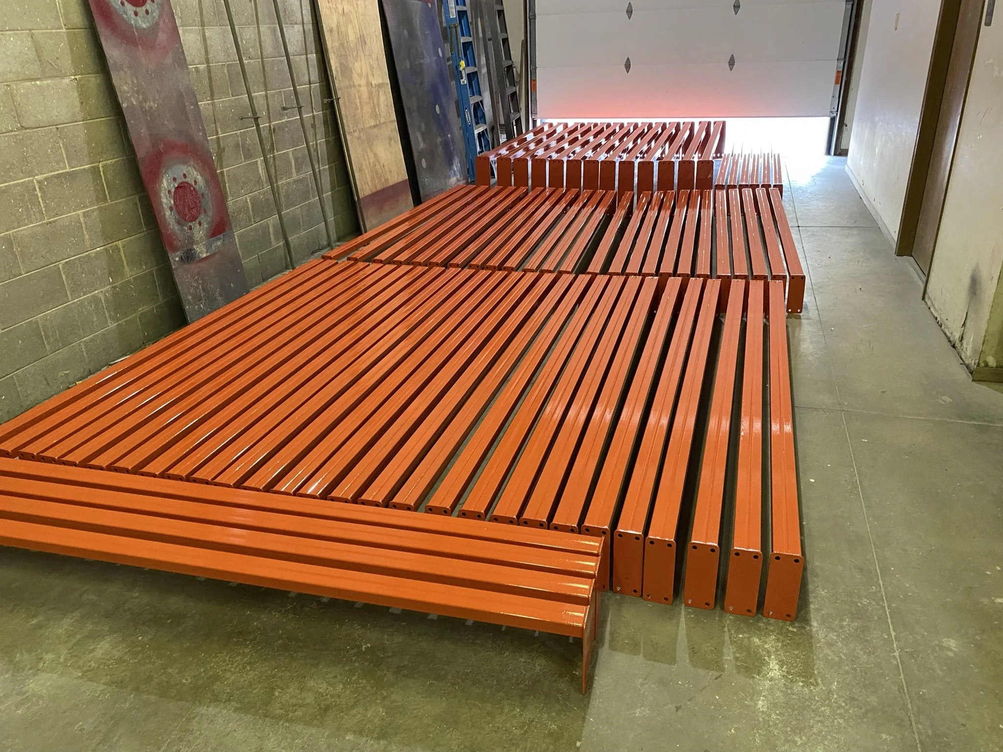 Multiple orange metal benches in a room with concrete floor, cinder block wall, and a partially open garage-style door in the background.