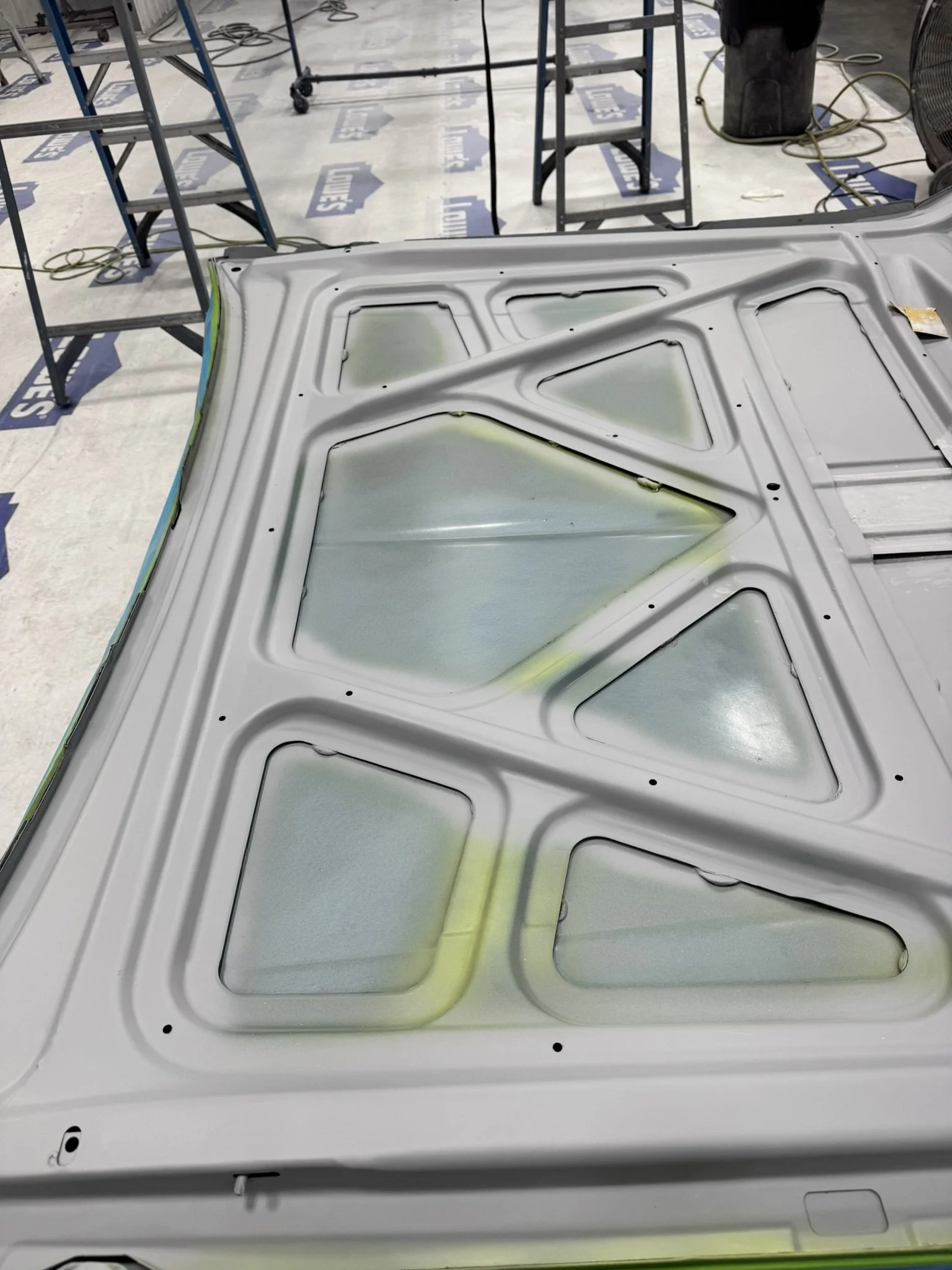 A metal panel with a geometric pattern on it, placed on a white surface in a workshop with equipment and tools around.