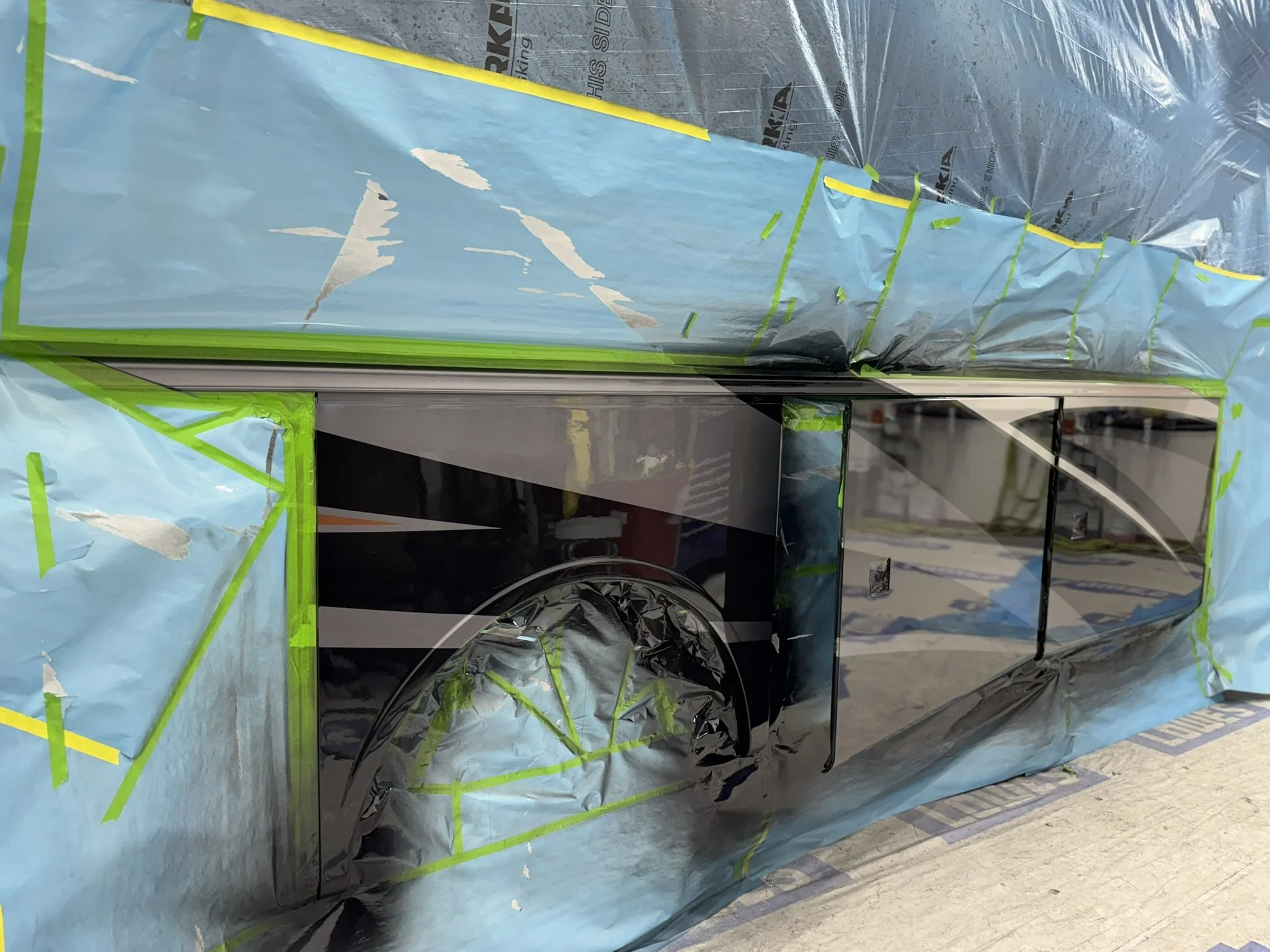 A car wrapped in a blue protective cover with green tape around it, parked inside a building with a tiled floor.