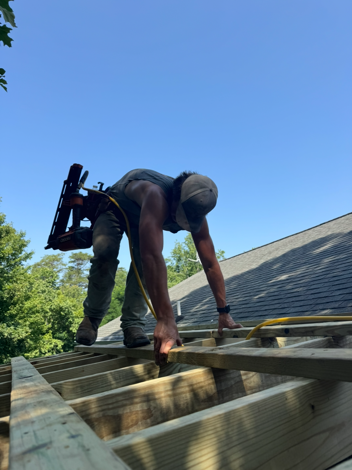 A person working on a roof, bending over, wearing a hat, with tools and materials around.