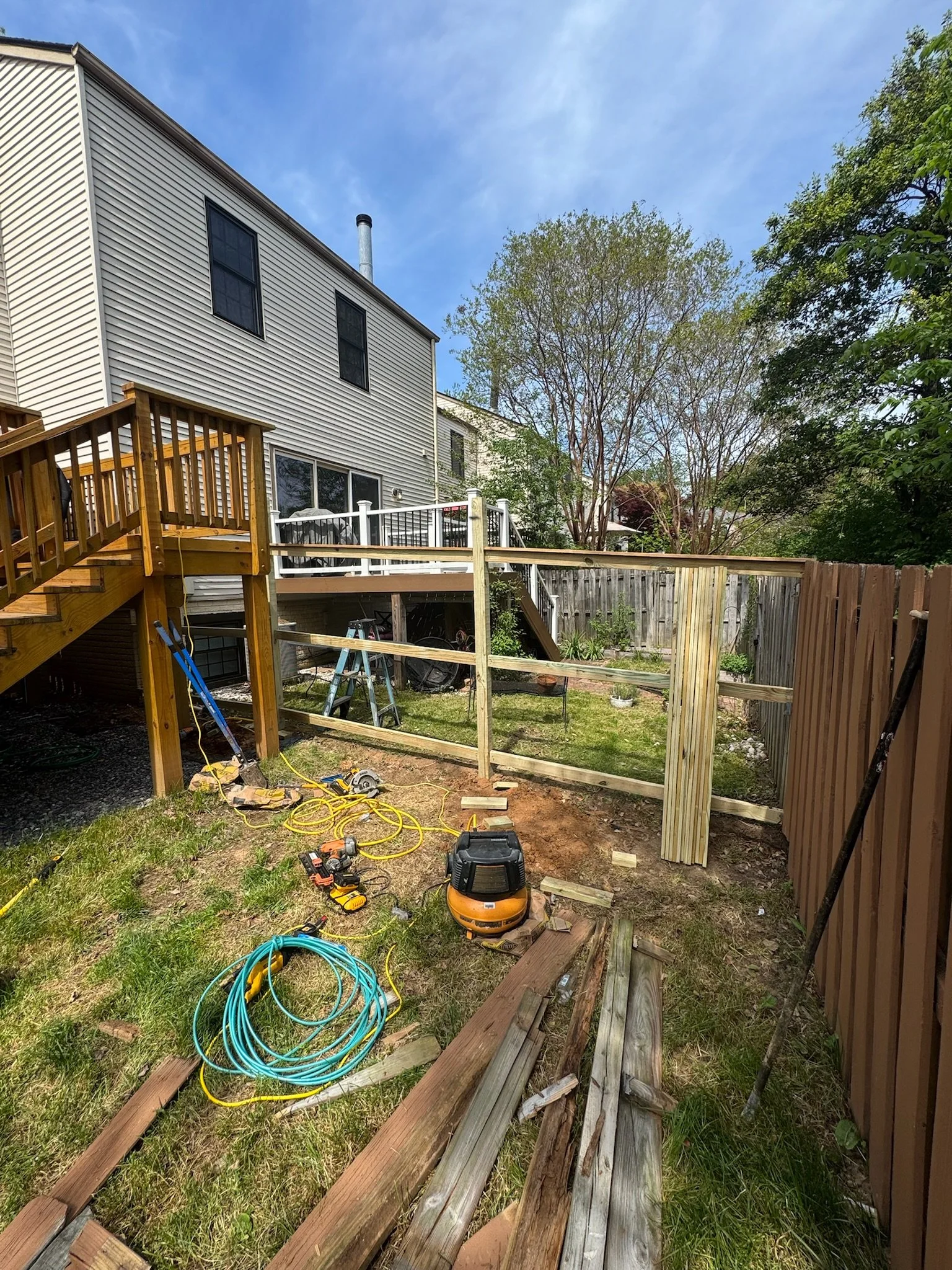 Backyard construction with wooden deck, tools, and fencing in progress on a sunny day.
