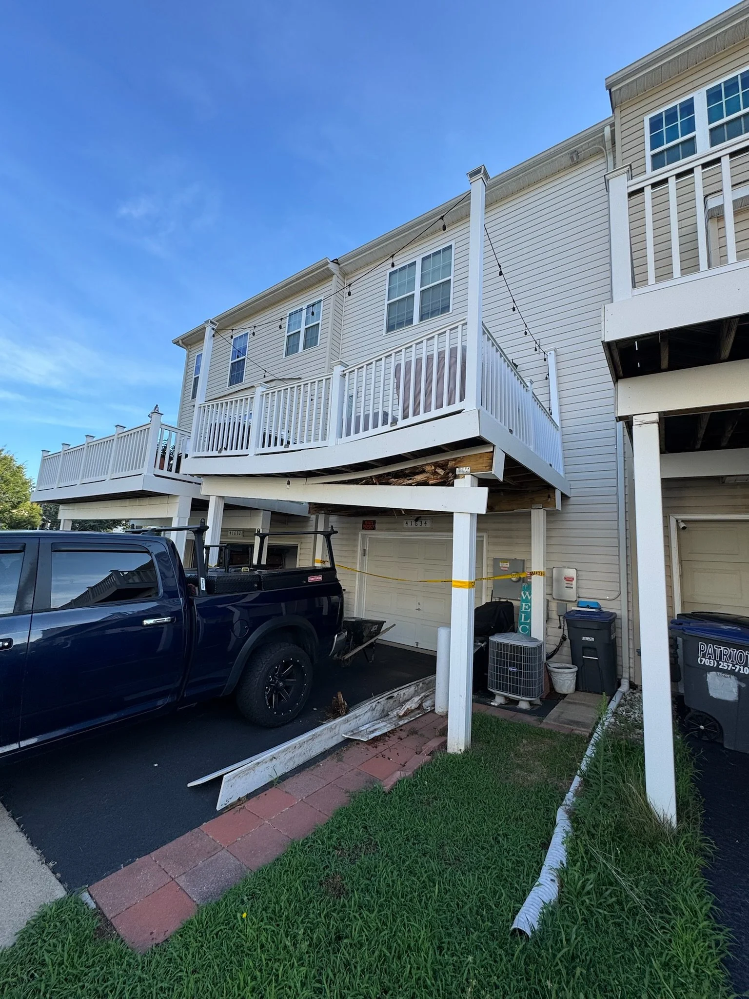 Apartment building with a damaged balcony and debris on the ground, parked truck in front, and a damaged white cable on the sidewalk.