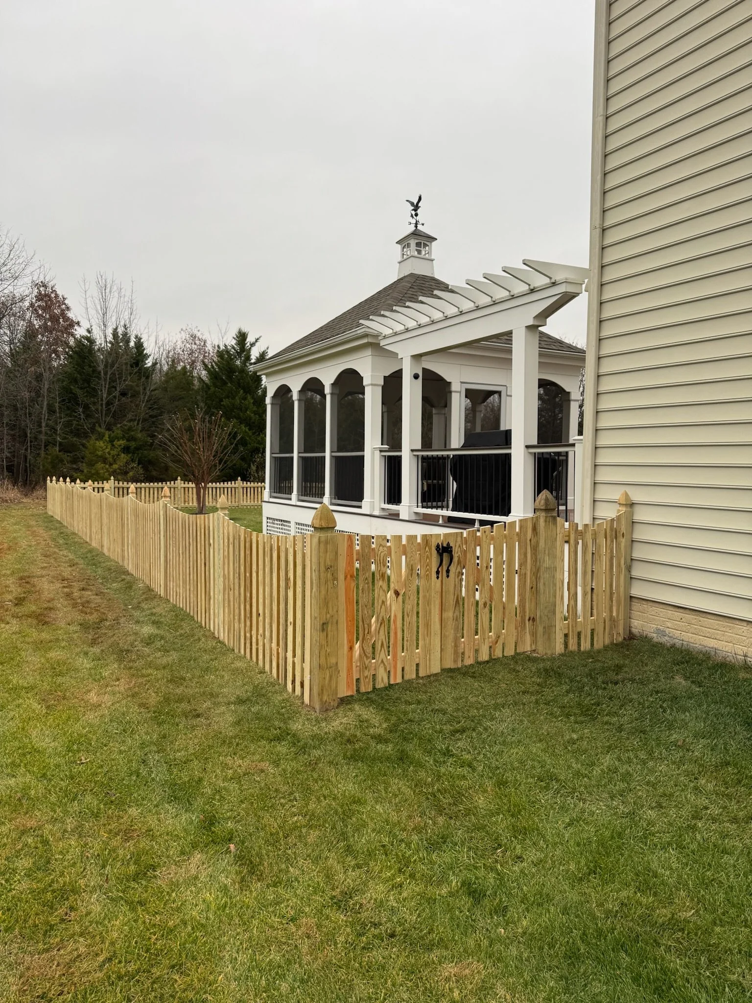 A backyard with a newly built wooden fence around a grassy yard, a screened porch attached to a house, and a cloudy sky overhead.