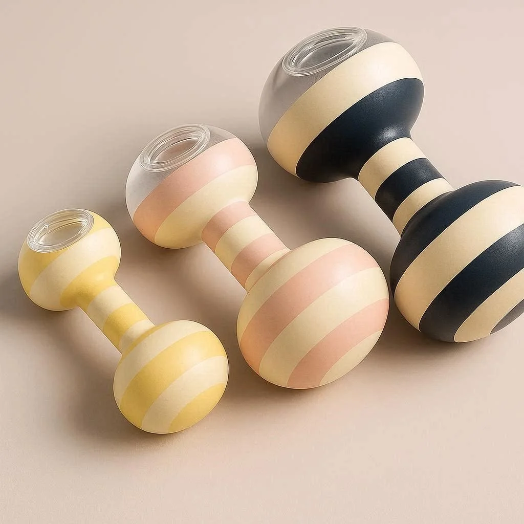 Three striped pool side, water fillable dumbbell-shaped objects in pastel yellow, pink, and black colors on a light beige background.