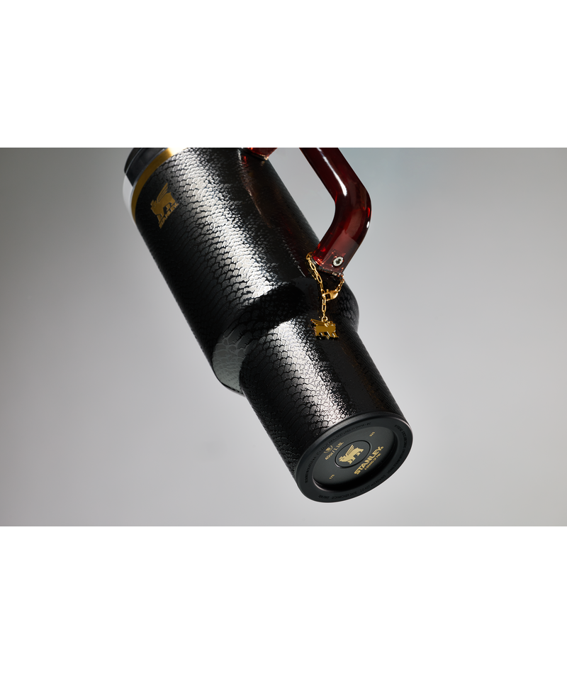 A black Stanley tumbler with a textured snake-skin pattern, with translucent color tritan handle and an electroformed charm.