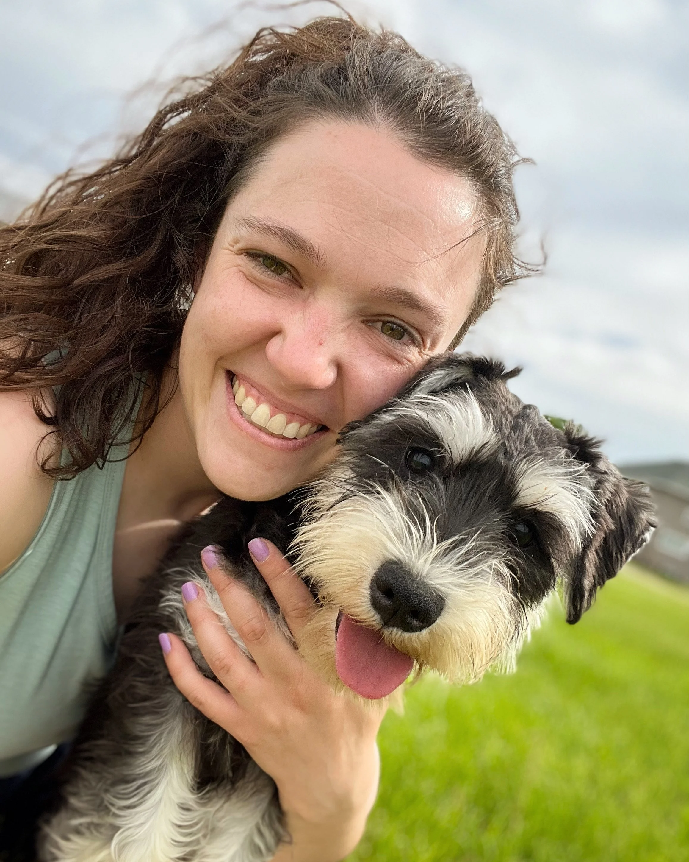 A woman smiles and holds a Miniature Schnauzer dog while outside