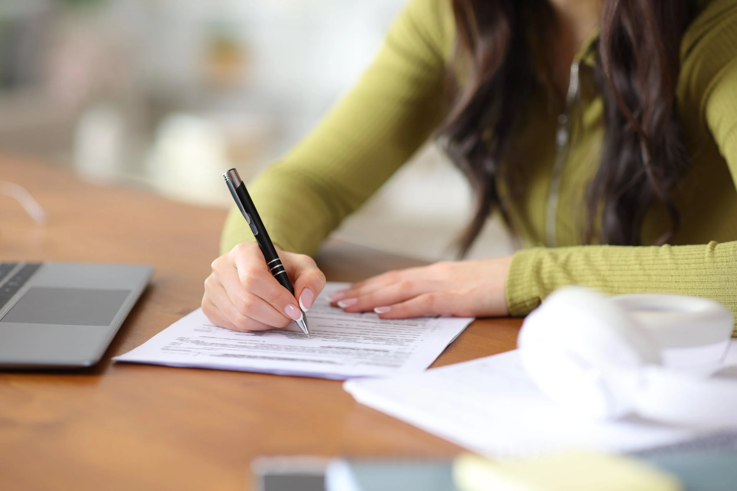 A woman's hands fills out paperwork on a desk with a pen