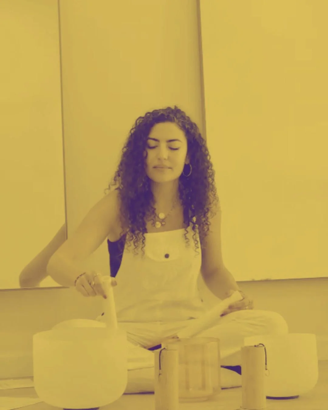A woman with curly hair sitting cross-legged on the floor, with her eyes closed, surrounded by candles.