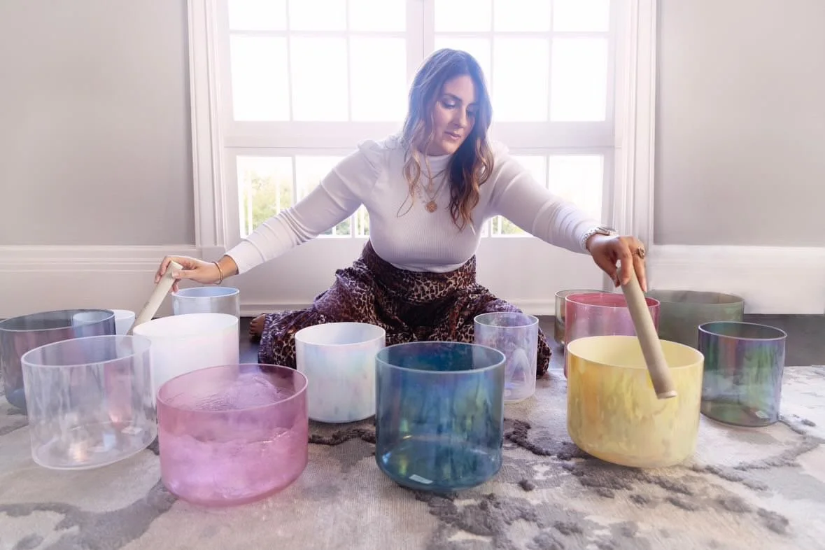 Woman playing colorful crystal singing bowls in a bright room.