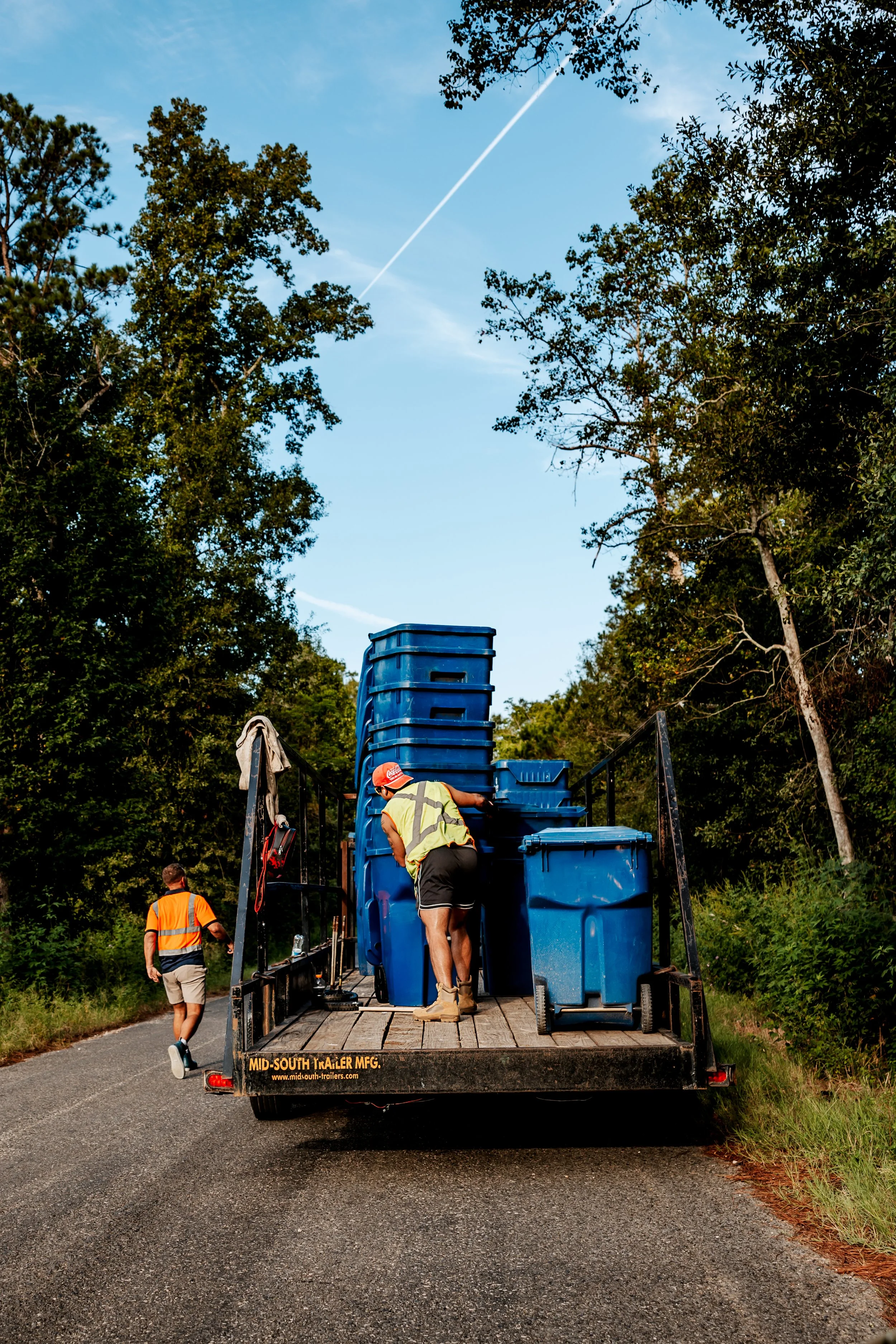 Workers loading blue residential carts onto an OnlyCans trailer