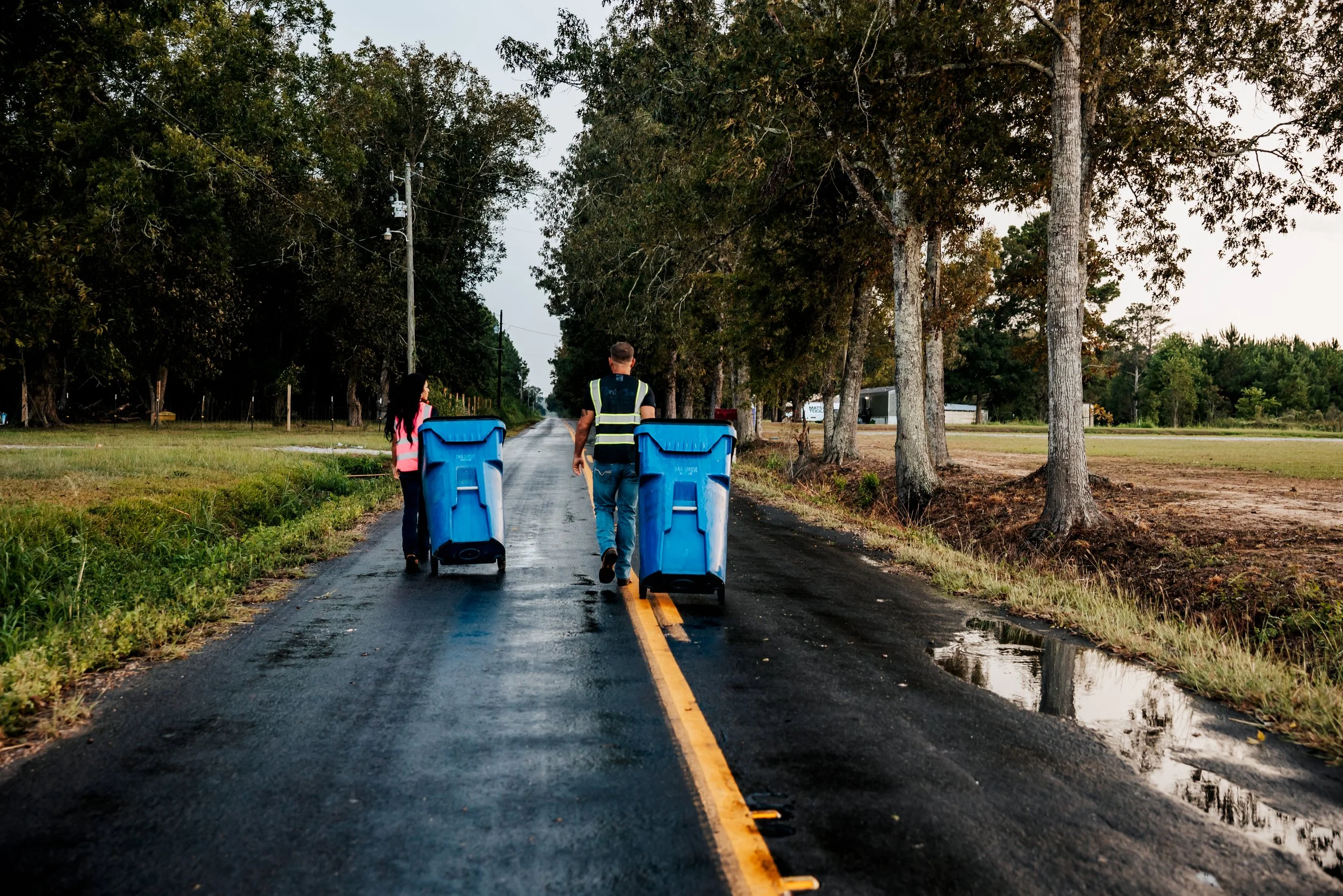 OnlyCans crew moving residential carts on a wet roadway