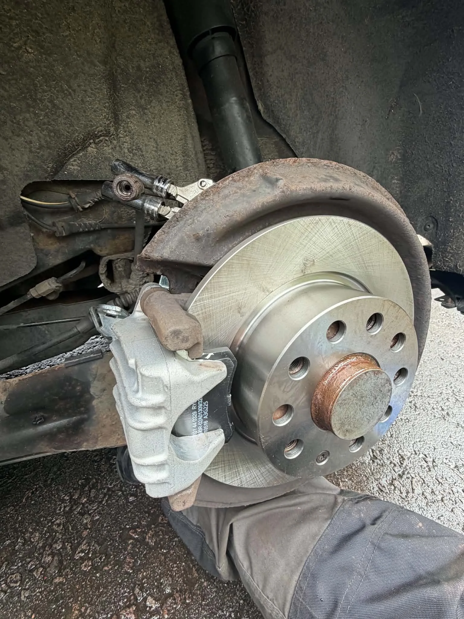 Close-up of a car wheel assembly in the process of repair or replacement, showing the brake rotor, caliper, and suspension components.