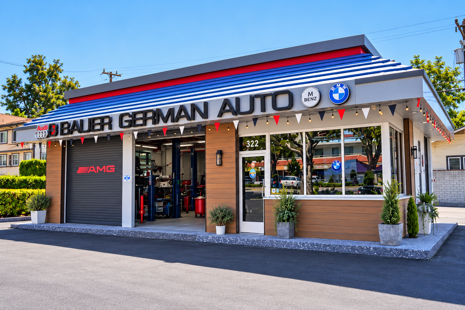 Exterior view of a car repair shop with signage for Bauer German Auto, featuring logos for Audi, BMW, Mercedes-Benz, and AMG, with a partially open garage door revealing automotive equipment inside, and potted plants outside.