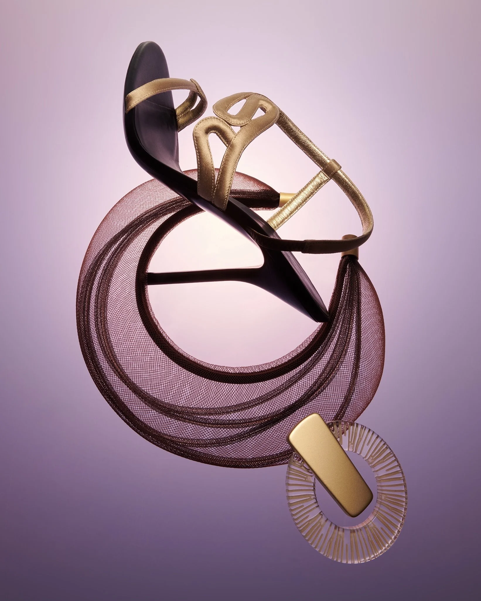 A decorative high-heeled sandal with gold straps, a pink mesh ribbon, and a gold rectangular embellishment, set against a soft purple background.