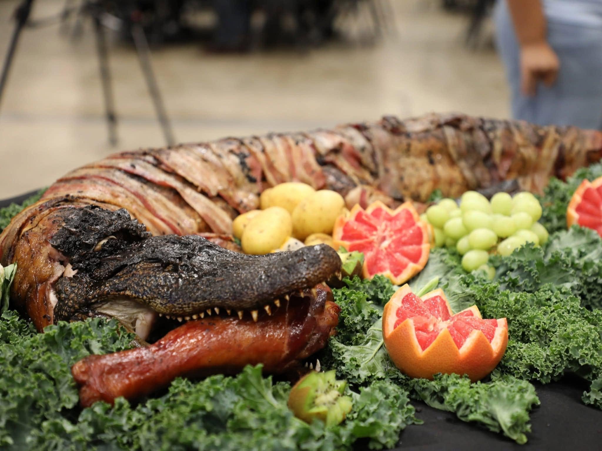 A roasted whole fish garnished for presentation, surrounded by sliced citrus fruits, grapes, and fresh greens.